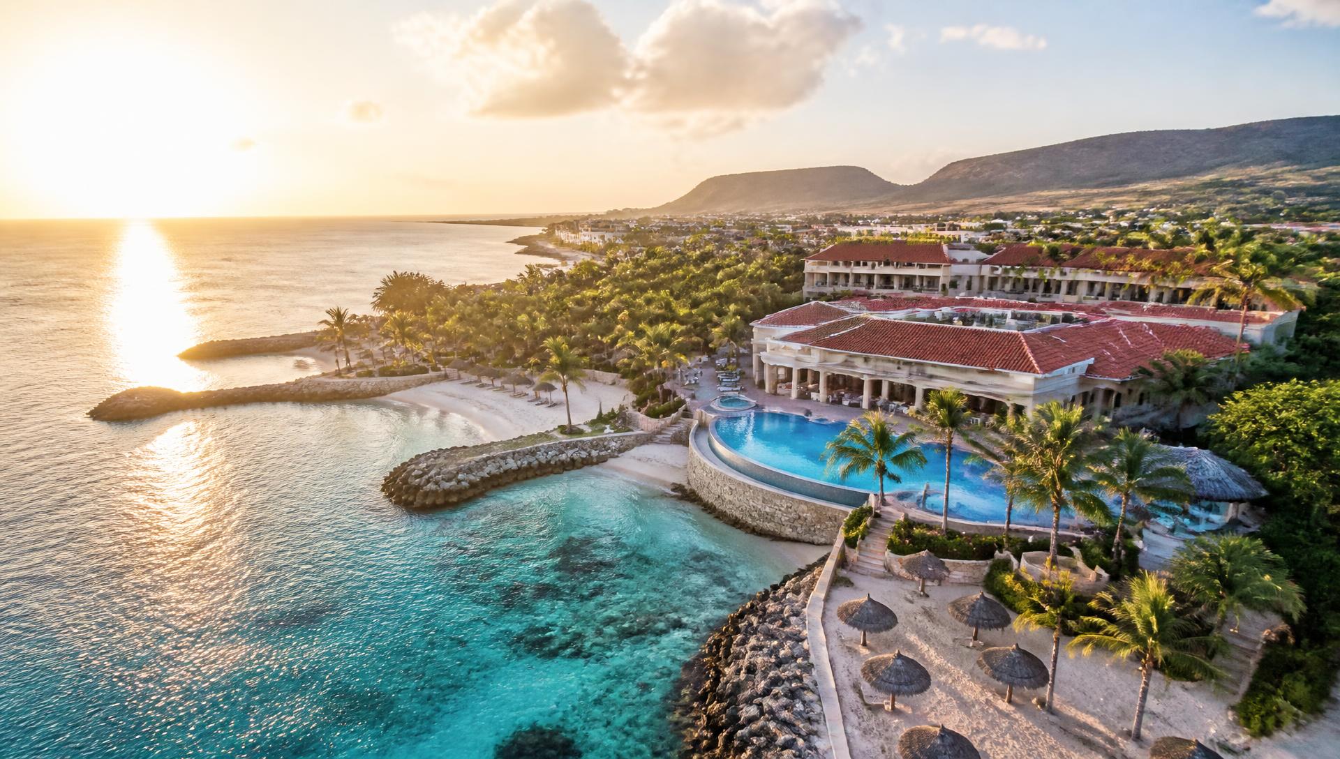 Zonsopkomst boven een luxe resort met palmbomen en turquoise zee op Curaçao